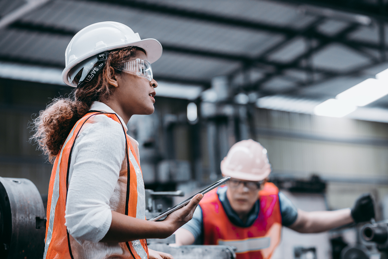 Female industrial engineer wearing a white helmet while standing in a heavy industrial factory behind she talking with workers, Various metal parts of the project (Female industrial engineer wearing a white helmet while standing in a heavy industrial 